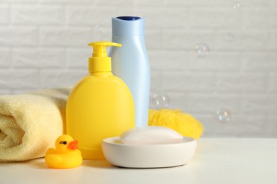 Photo of Baby cosmetic products, bath duck, sponge and towel on white table against soap bubbles. Space for text
