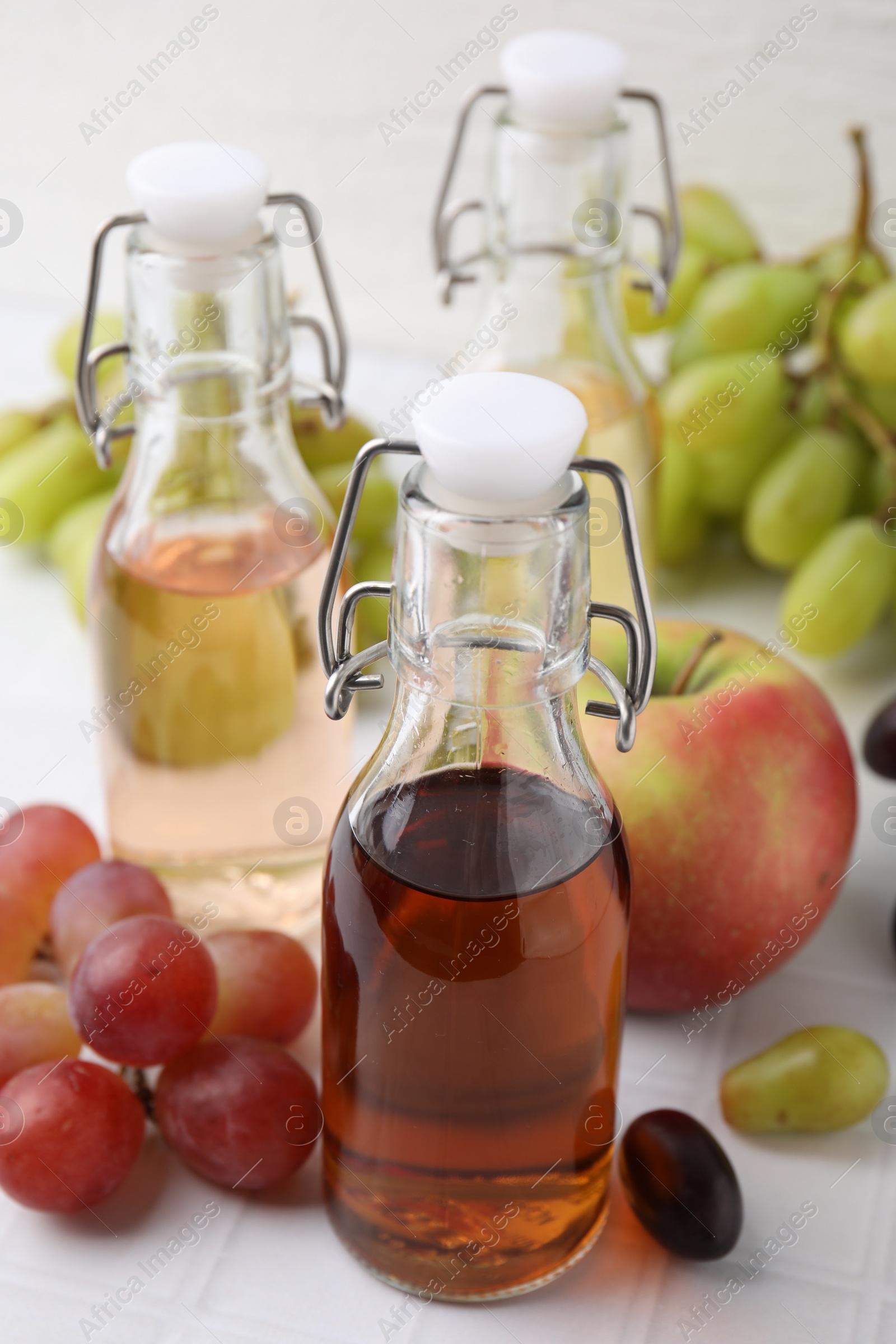 Photo of Different types of vinegar and ingredients on light tiled table, closeup