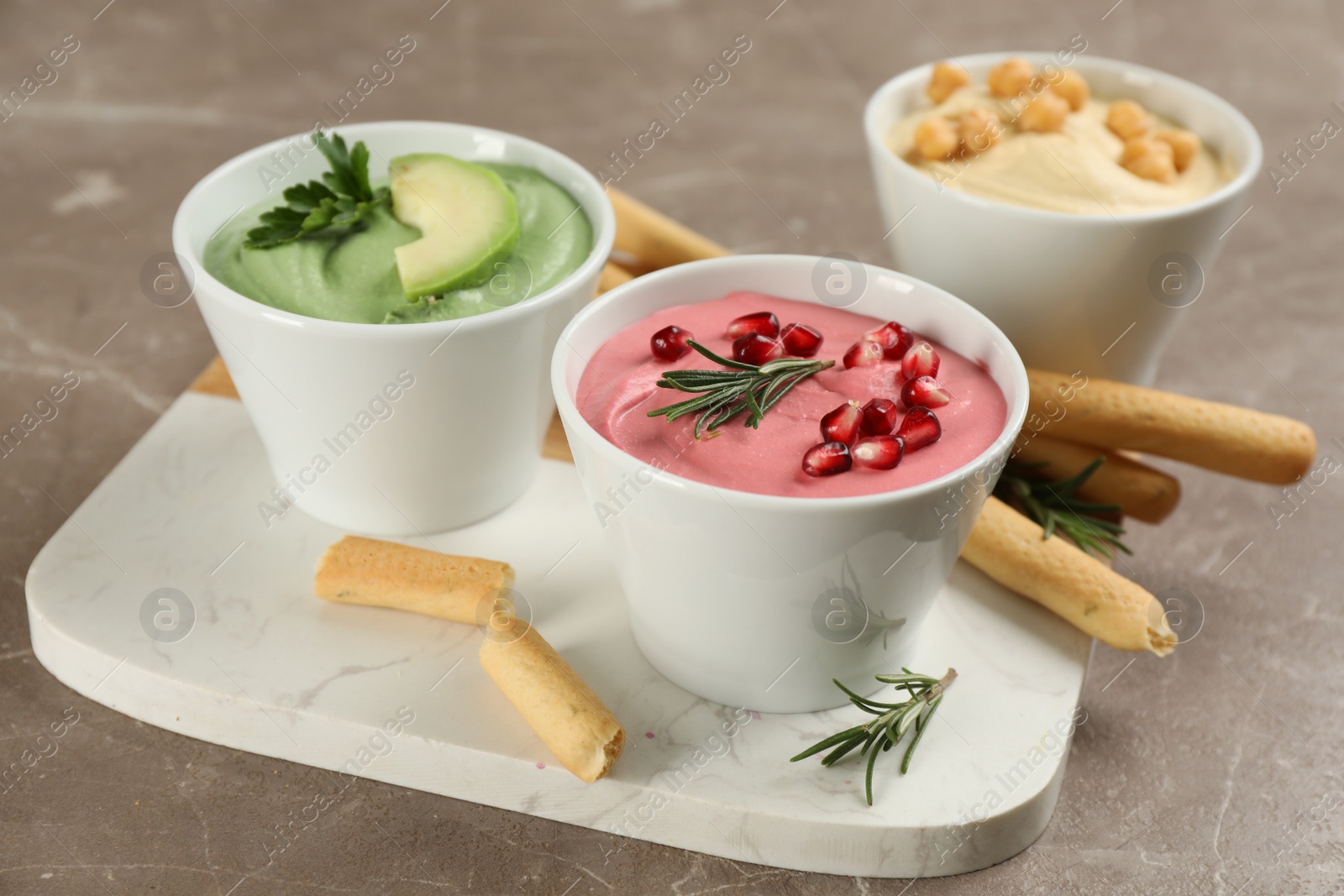 Photo of Different delicious hummuses with bread sticks on brown marble table