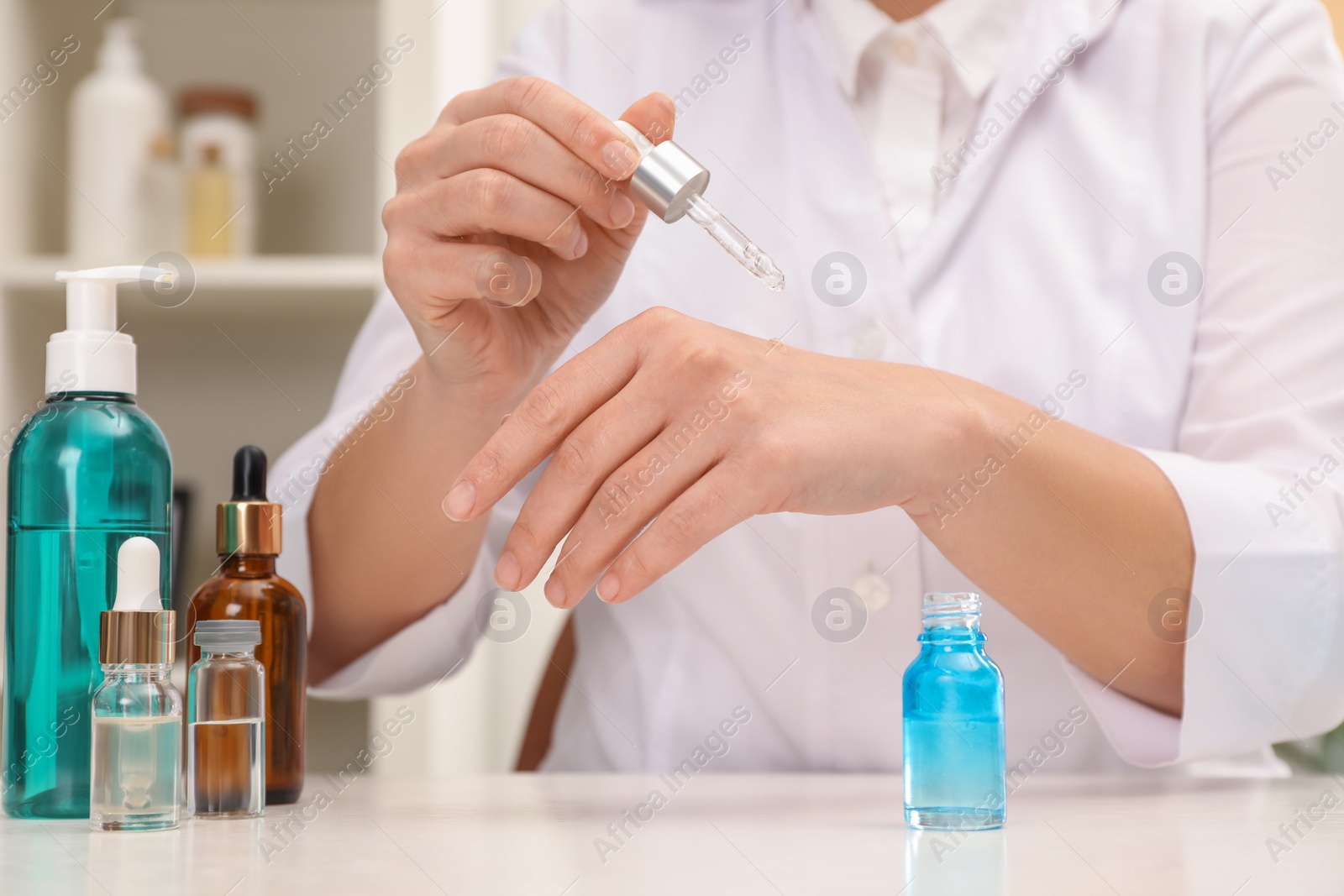 Photo of Dermatologist testing cosmetic product at white table indoors, closeup