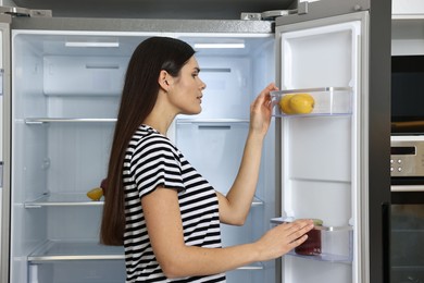 Photo of Upset woman near empty refrigerator in kitchen