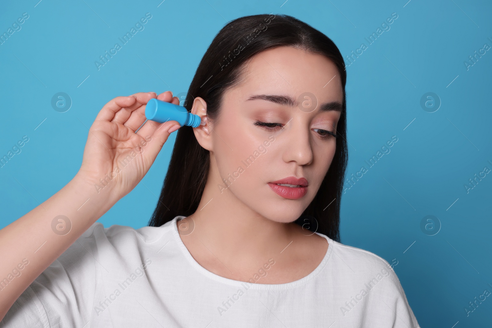Photo of Young woman using ear drops on light blue background