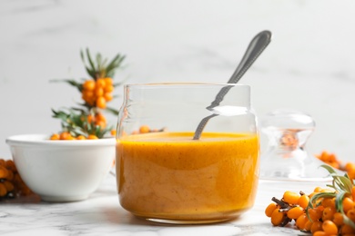 Photo of Delicious sea buckthorn jam and fresh berries on white marble table