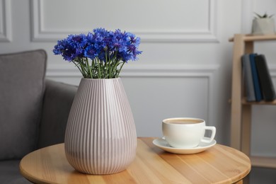 Photo of Beautiful cornflowers in vase and cup of coffee on wooden table at home