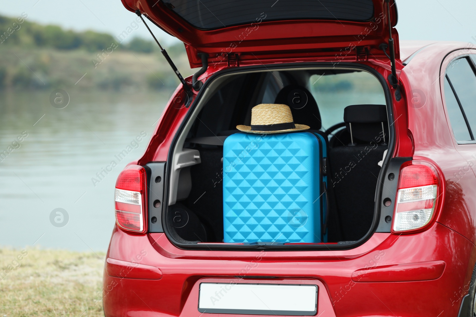 Photo of Suitcase and hat in car trunk on riverside, closeup