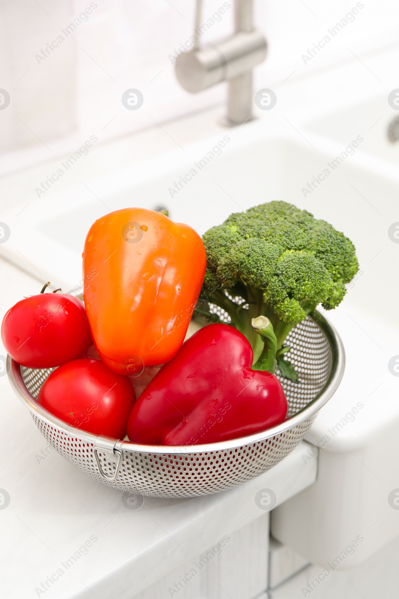 Photo of Fresh clean vegetables in colander on countertop near sink