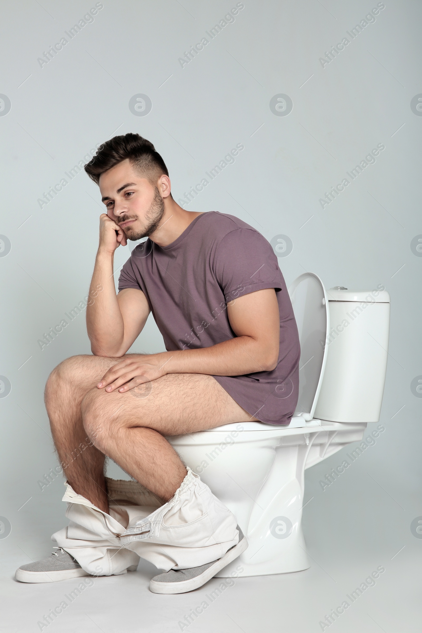 Photo of Young man sitting on toilet bowl against gray background