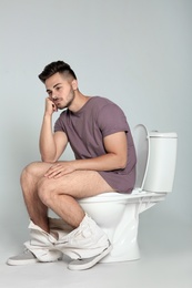 Young man sitting on toilet bowl against gray background