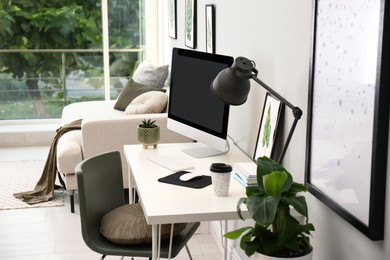 Comfortable workplace with modern computer and houseplants in room. Interior design