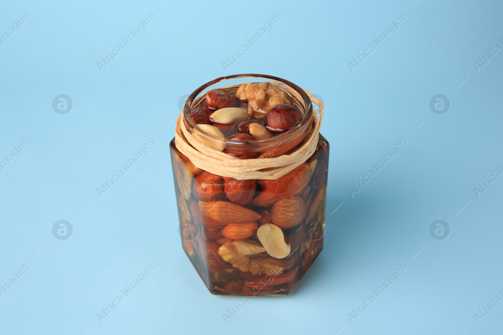 Photo of Jar with different delicious nuts and honey on light blue background