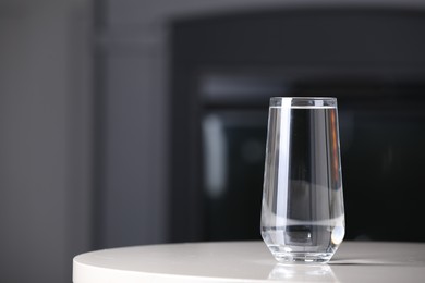 Glass of clean water on white table indoors, space for text