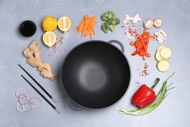 Photo of Wok, chopsticks and different products on grey table, flat lay