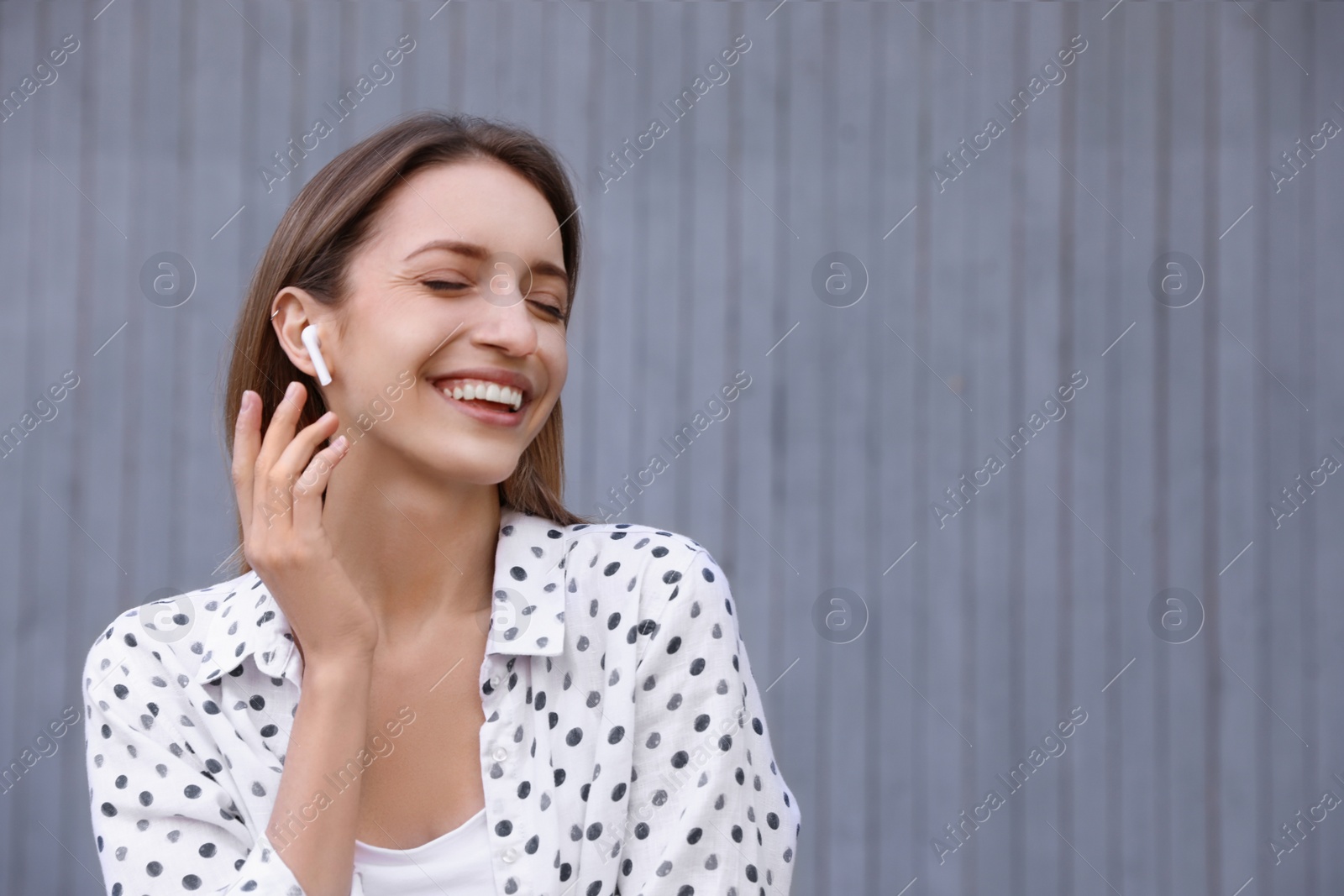 Photo of Young woman with wireless headphones listening to music near grey wall. Space for text