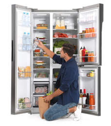Photo of Man with bag of groceries near open refrigerator on white background
