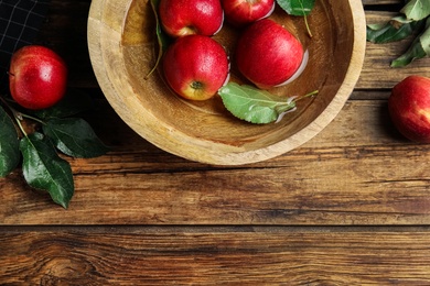 Photo of Ripe red apples in bowl of water on wooden table, flat lay. Space for text