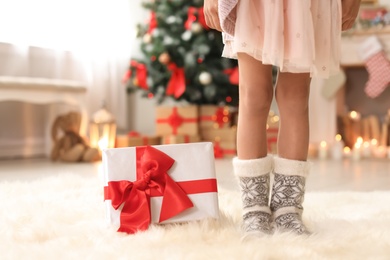 Cute little child in warm socks with Christmas gift box at home