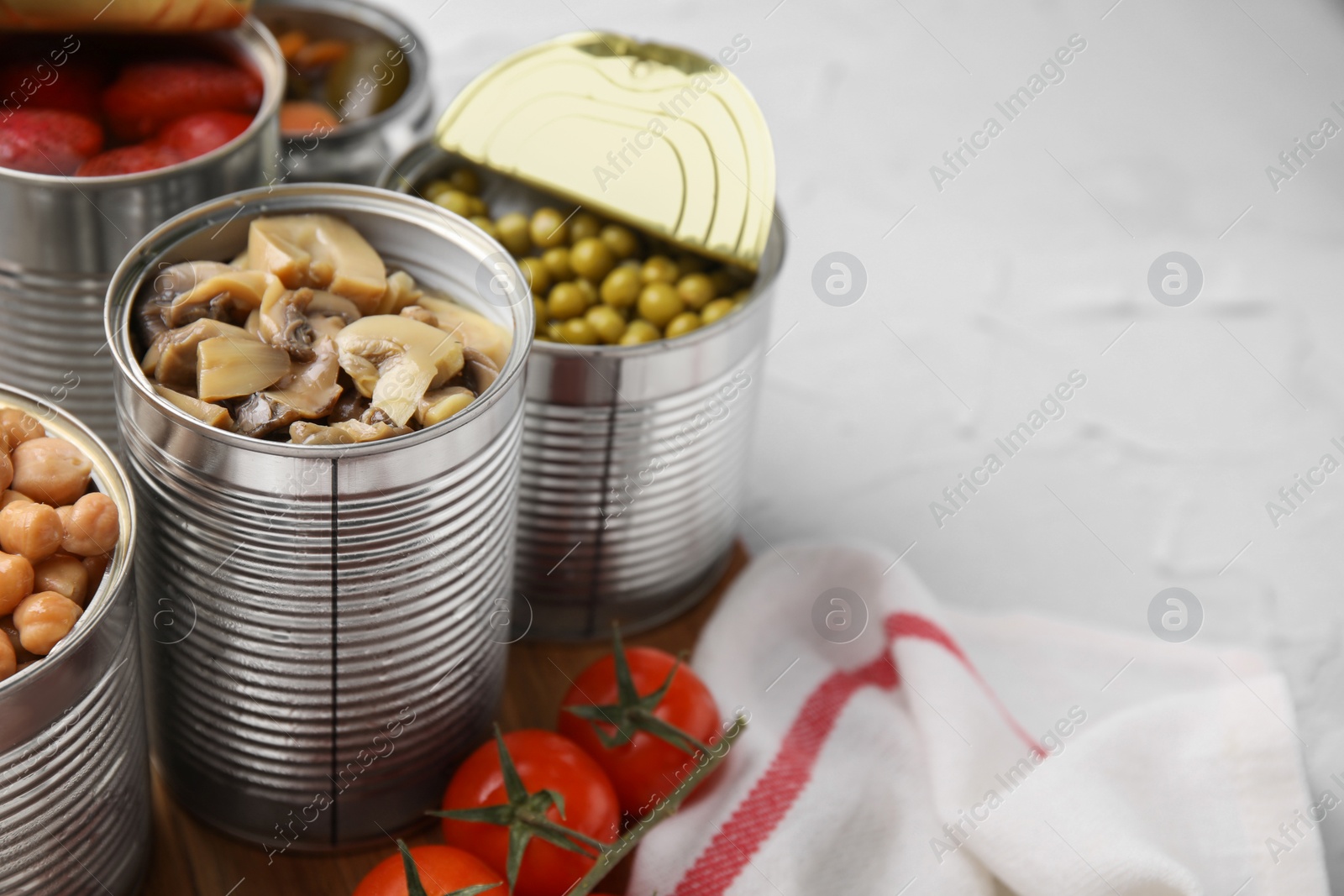 Photo of Open tin cans with different preserved products on white textured table, closeup. Space for text