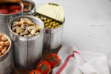 Open tin cans with different preserved products on white textured table, closeup. Space for text