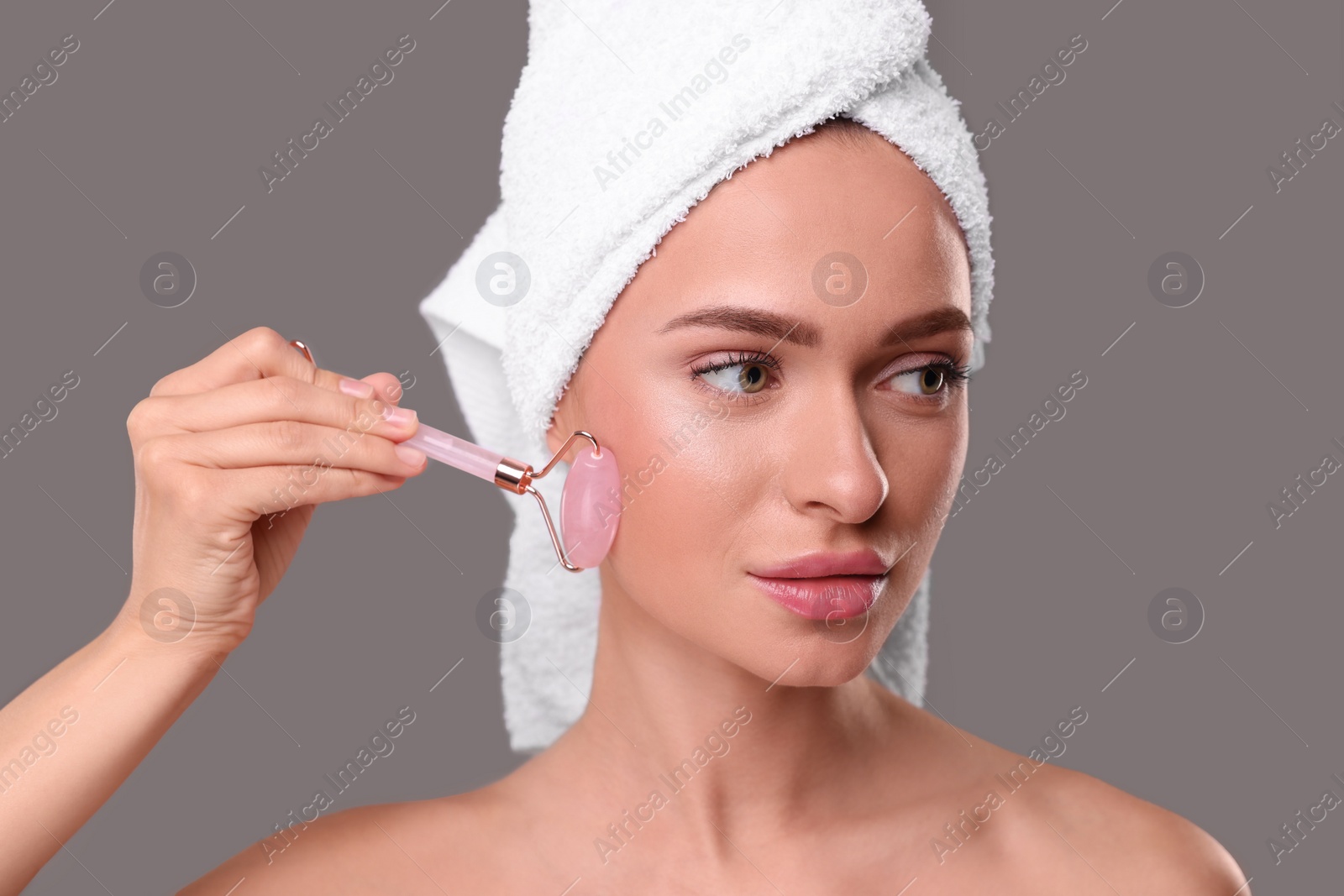 Photo of Young woman massaging her face with rose quartz roller on grey background