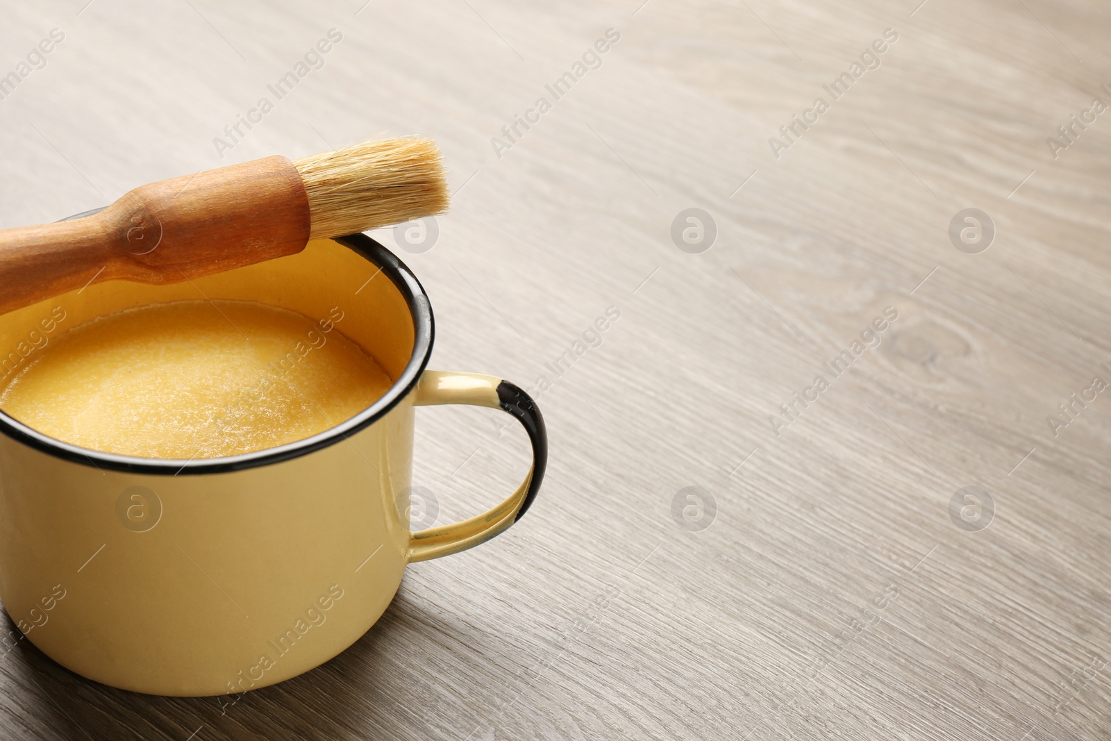 Photo of Mug of melting butter with brush on wooden table. Space for text