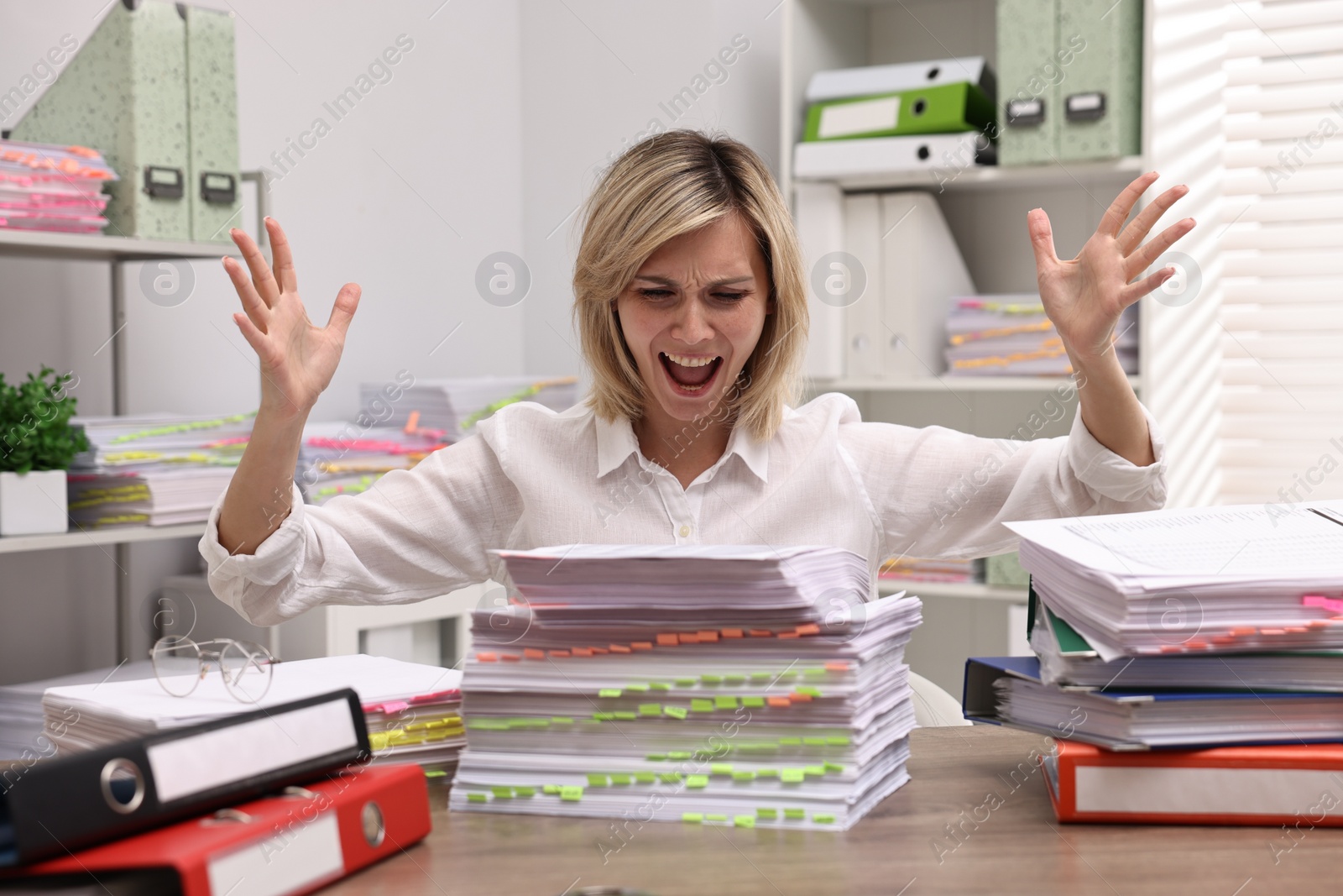 Photo of Overwhelmed woman surrounded by documents at workplace in office