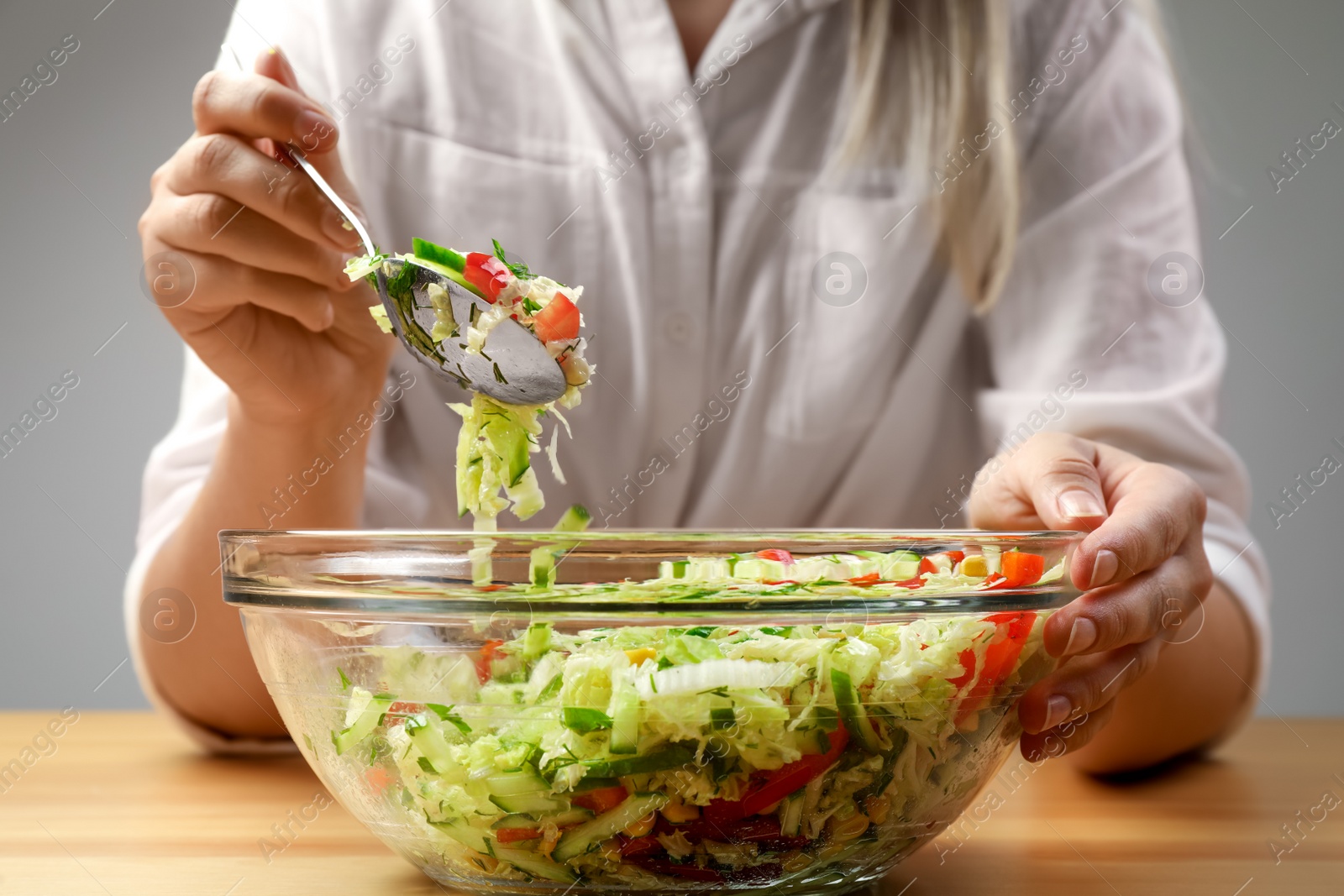 Photo of Woman making tasty salad with Chinese cabbage at wooden table, closeup