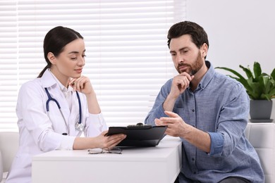 Doctor with clipboard consulting patient during appointment in clinic