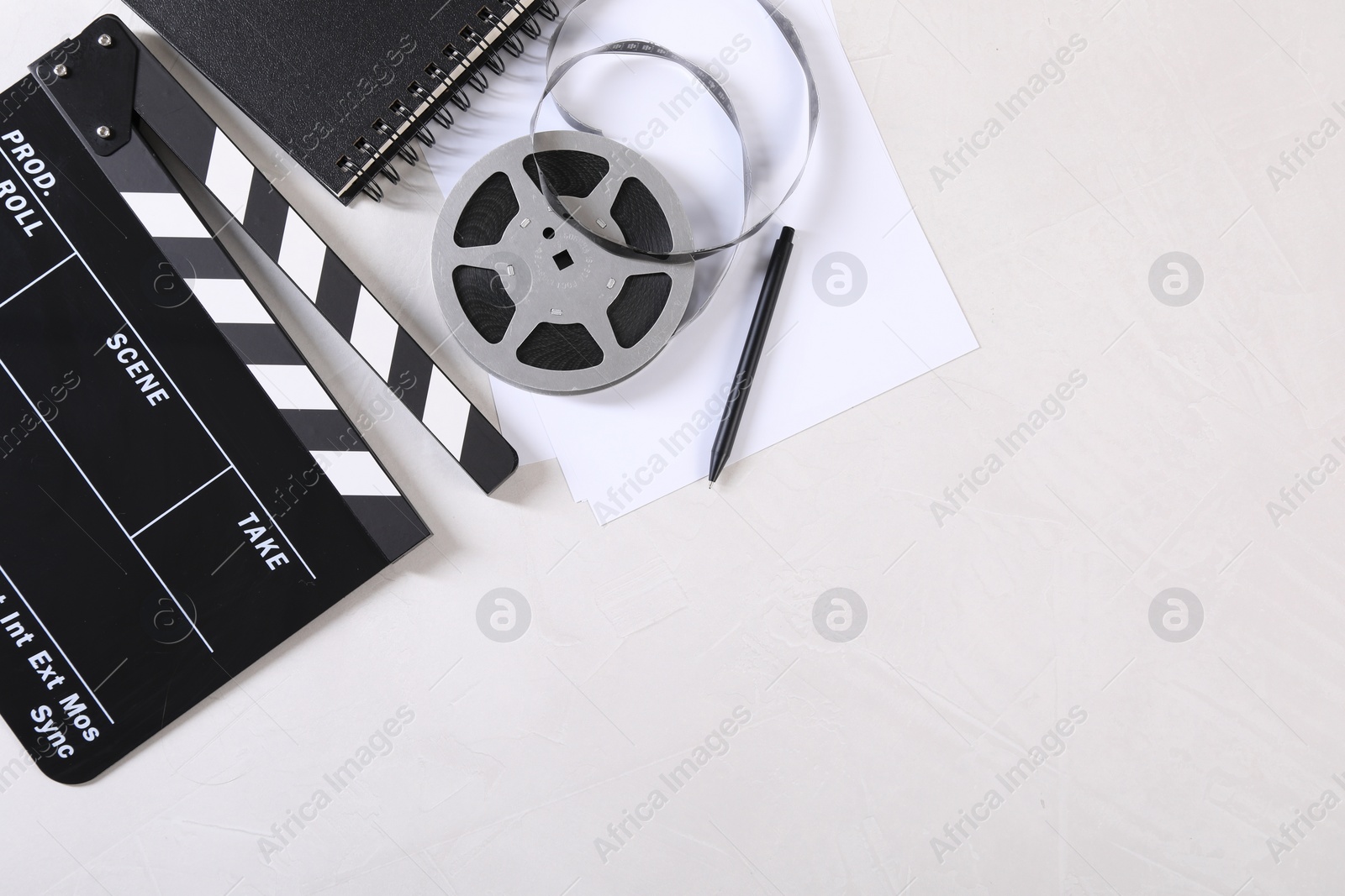 Photo of Movie clapper, film reel, notebook, sheet and pen on light textured table, flat lay. Space for text