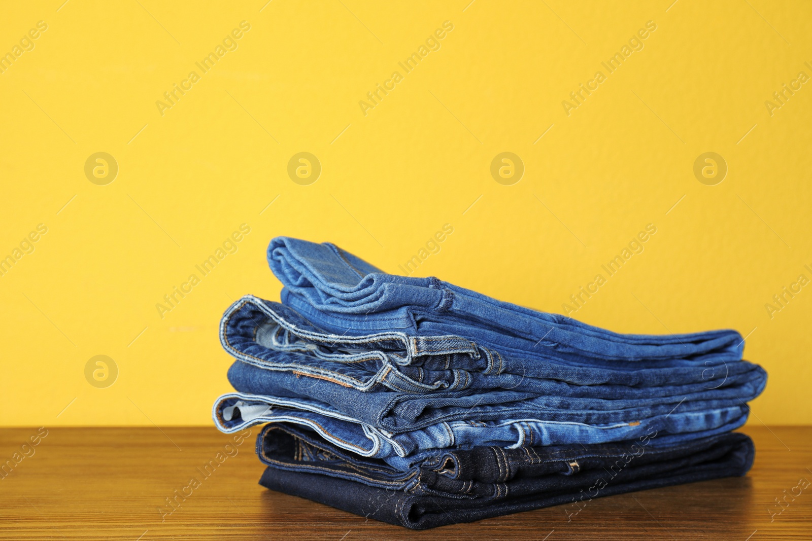 Photo of Stack of jeans on table against color background