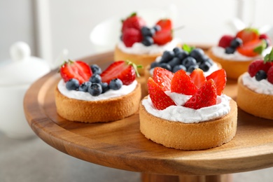 Photo of Cake stand with different berry tarts on table. Delicious pastries