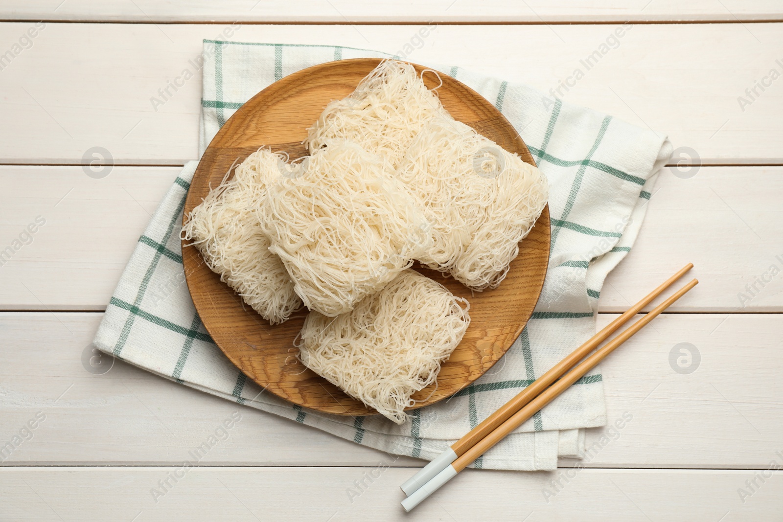 Photo of Plate with uncooked rice noodles and chopsticks on white wooden table, flat lay