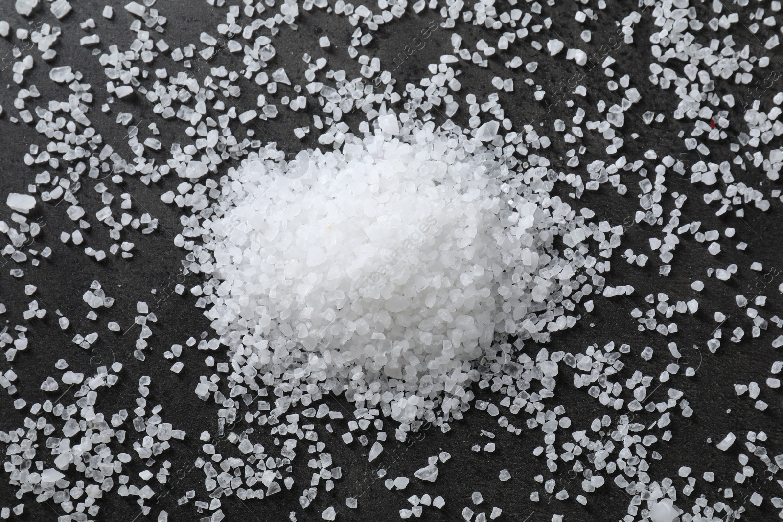 Photo of Heap of natural salt on black table, top view