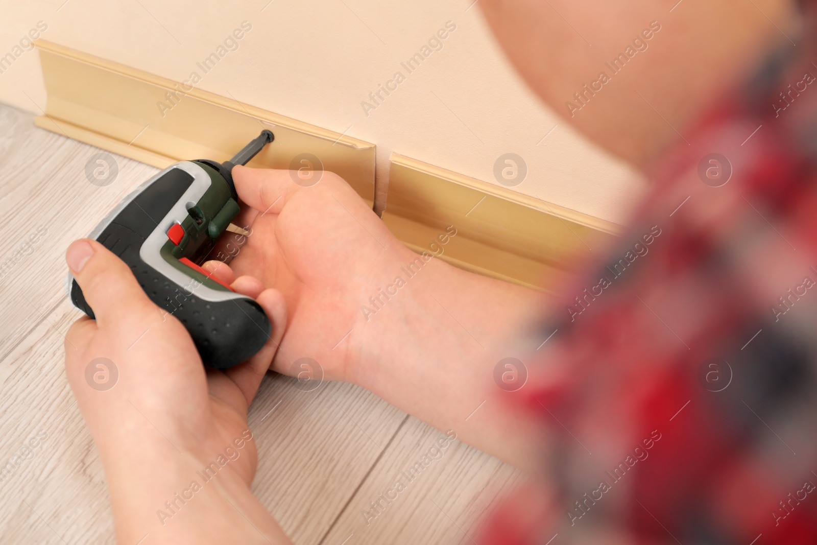 Photo of Man installing plinth on laminated floor with screwdriver in room, closeup