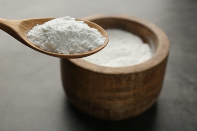 Spoon of baking powder over bowl at grey textured table, closeup. Space for text