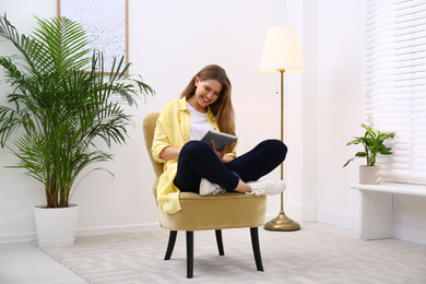 Photo of Young woman with tablet resting in armchair at home