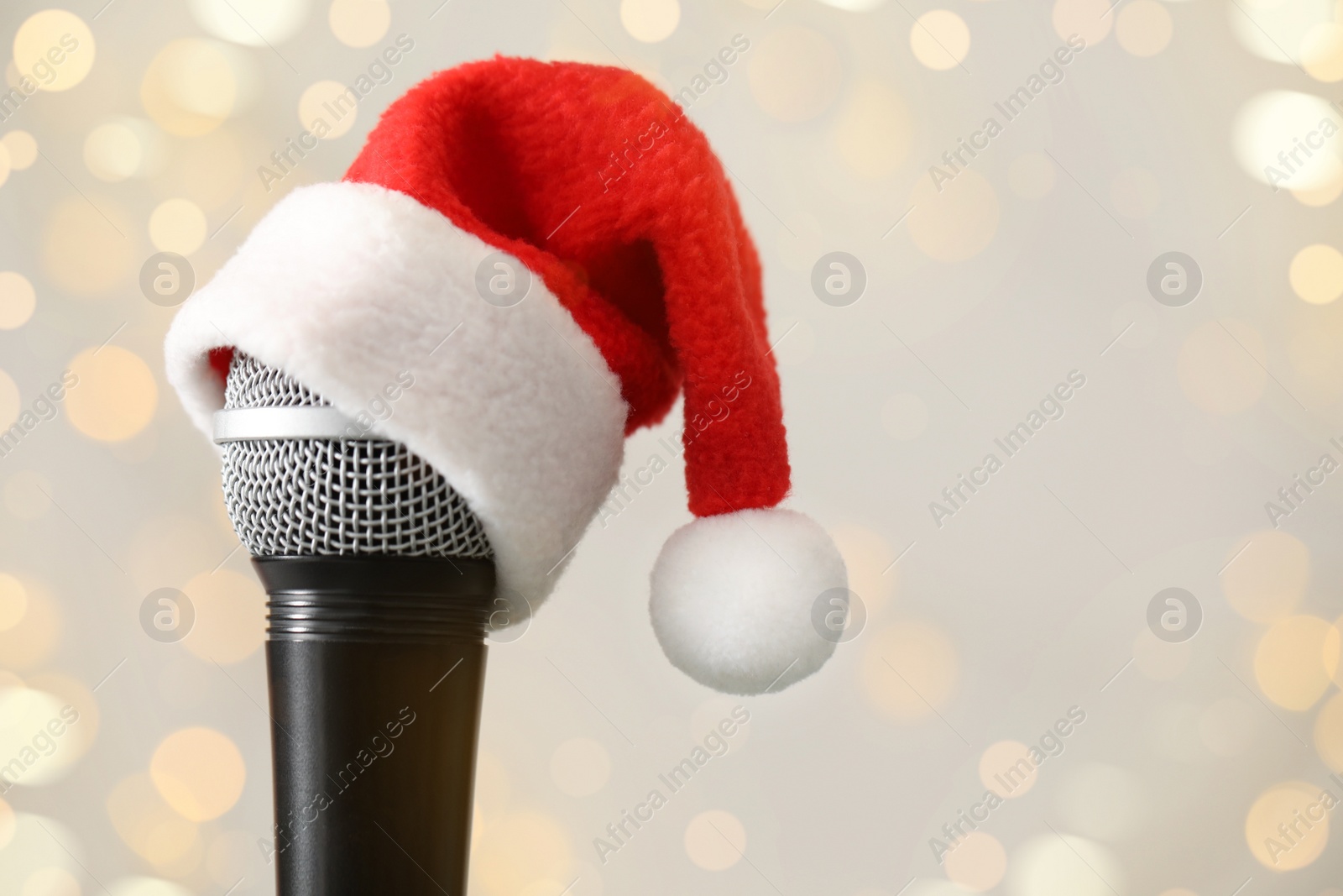 Photo of Microphone with Santa hat against blurred lights, space for text. Christmas music