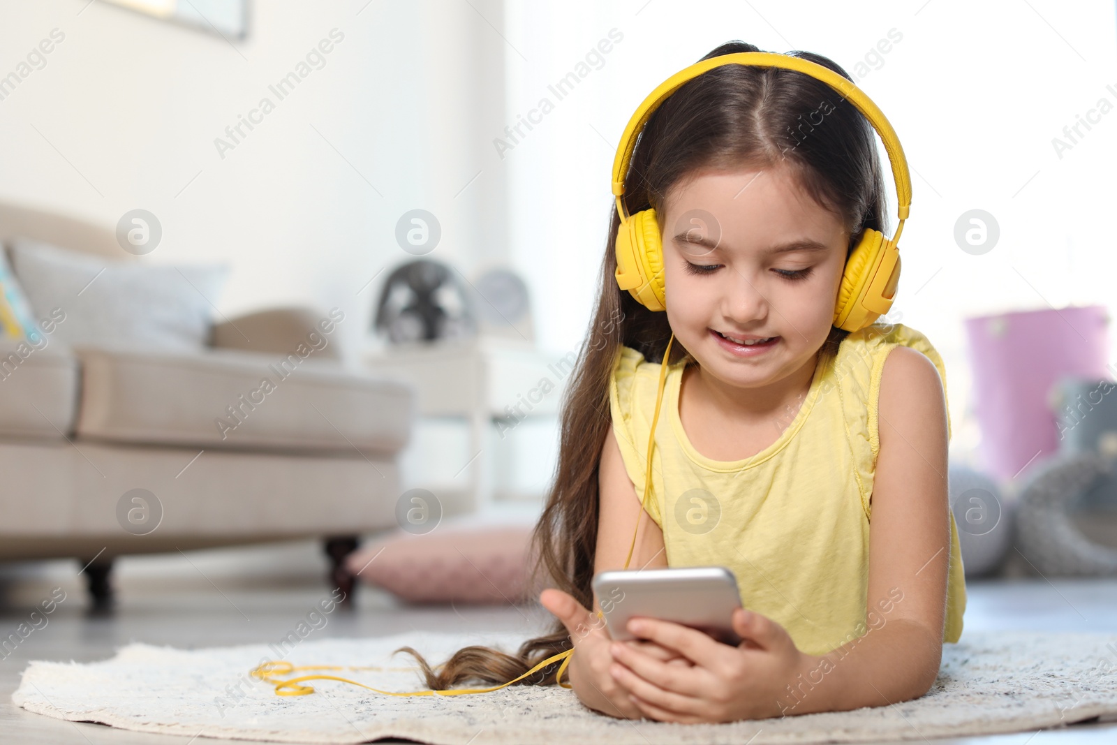 Photo of Cute child with headphones and mobile phone on floor indoors. Space for text