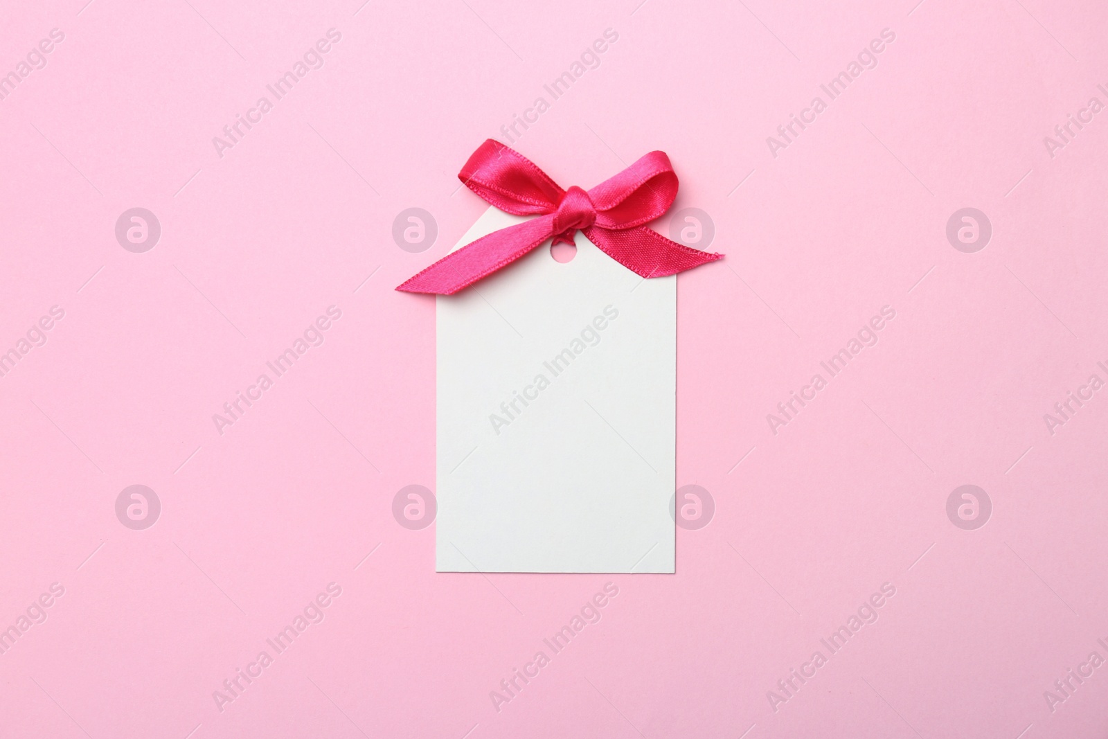 Photo of Blank gift tag with satin ribbon on color background, top view