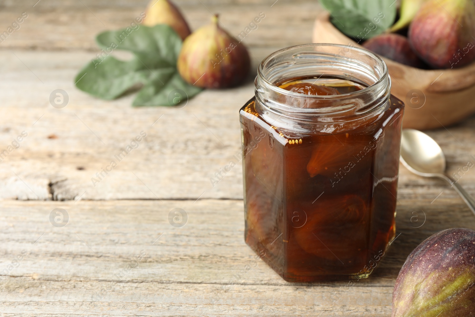 Photo of Jar of tasty sweet jam and fresh figs on wooden table. Space for text