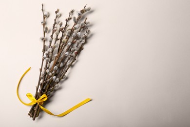 Photo of Beautiful blooming willow branches tied with yellow ribbon on beige background, top view. Space for text
