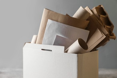 Photo of Box with different waste paper on grey table, closeup