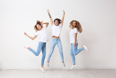 Group of young women in jeans jumping near light wall