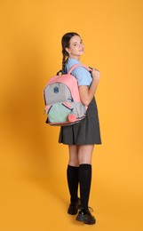 Photo of Teenage girl in school uniform with backpack on orange background