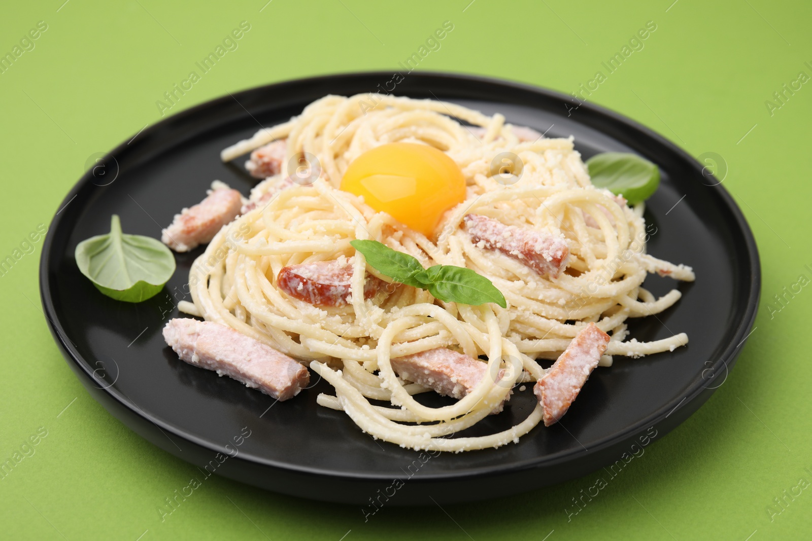 Photo of Plate of tasty pasta Carbonara with basil leaves on light green background, closeup