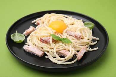 Photo of Plate of tasty pasta Carbonara with basil leaves on light green background, closeup