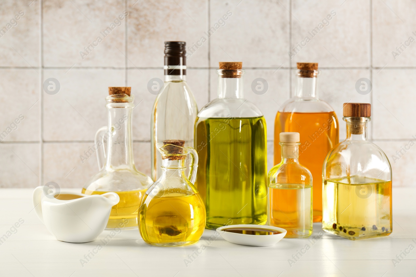 Photo of Vegetable fats. Different oils in glass bottles and dishware on white wooden table against tiled wall