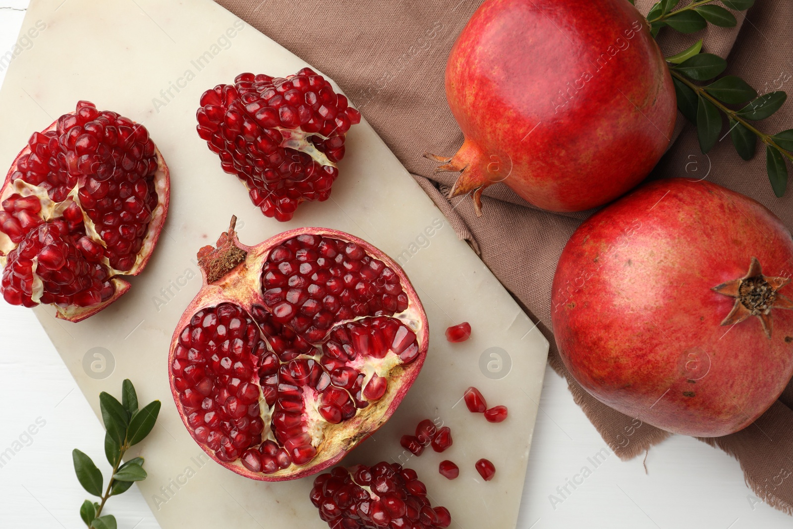 Photo of Fresh pomegranates and branches on white table, flat lay