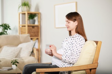 Photo of Beautiful pregnant woman holding pill and glass of water at home