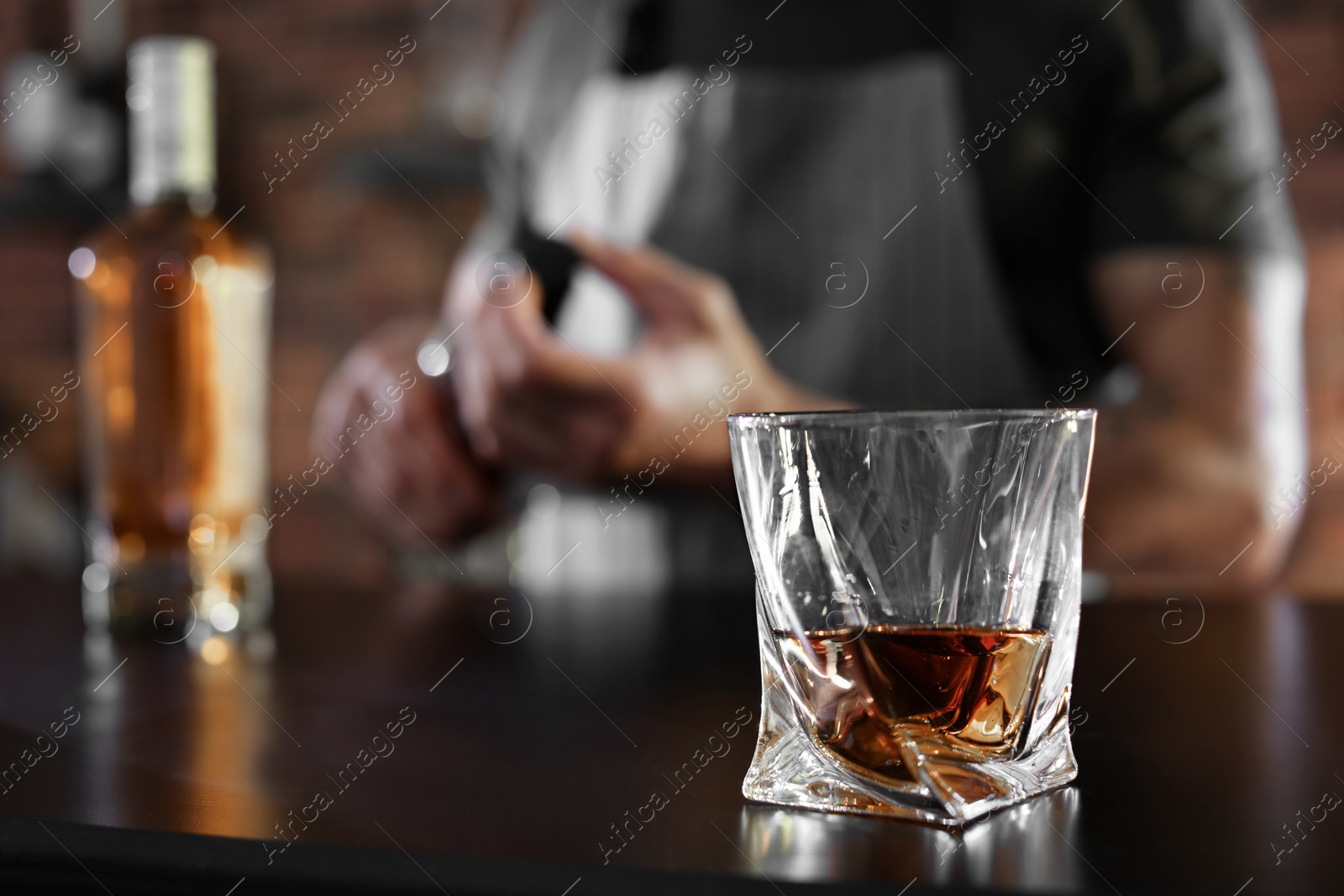 Photo of Bartender at counter with bottles and glass of whiskey in bar, closeup. Space for text