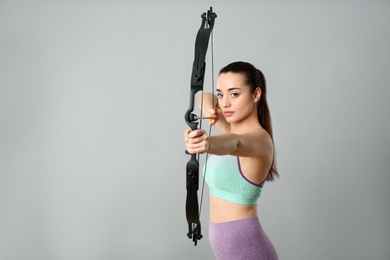 Young woman practicing archery on light grey background. Space for text